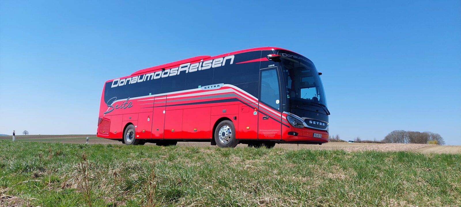 Donaumoos Reisen Setra-Reisebus auf Landstraße durch frühjahrshelle Felder