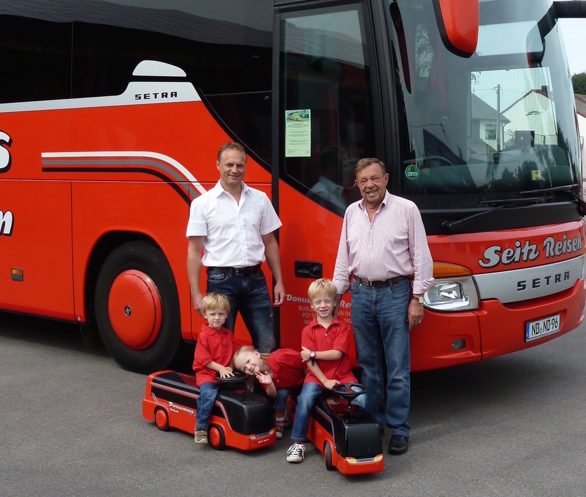Helmut Seitz mit Familie und Enkeln vor dem roten Setra-Reisebus von Seitz Reisen